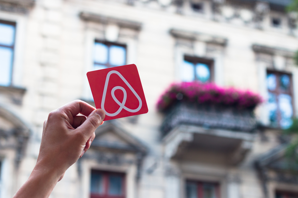 Hand holding Airbnb logo in front of building