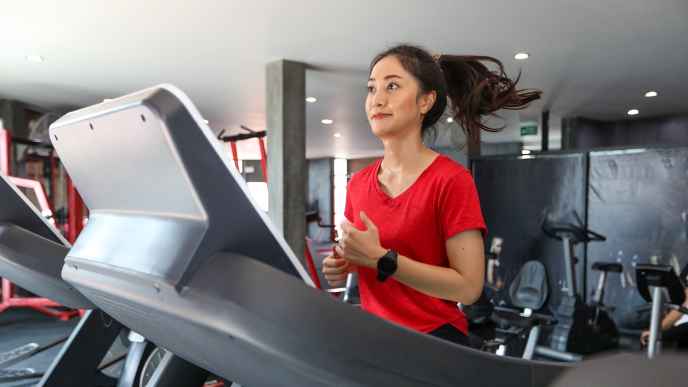 Woman in red shirt running on treadmill at gym.