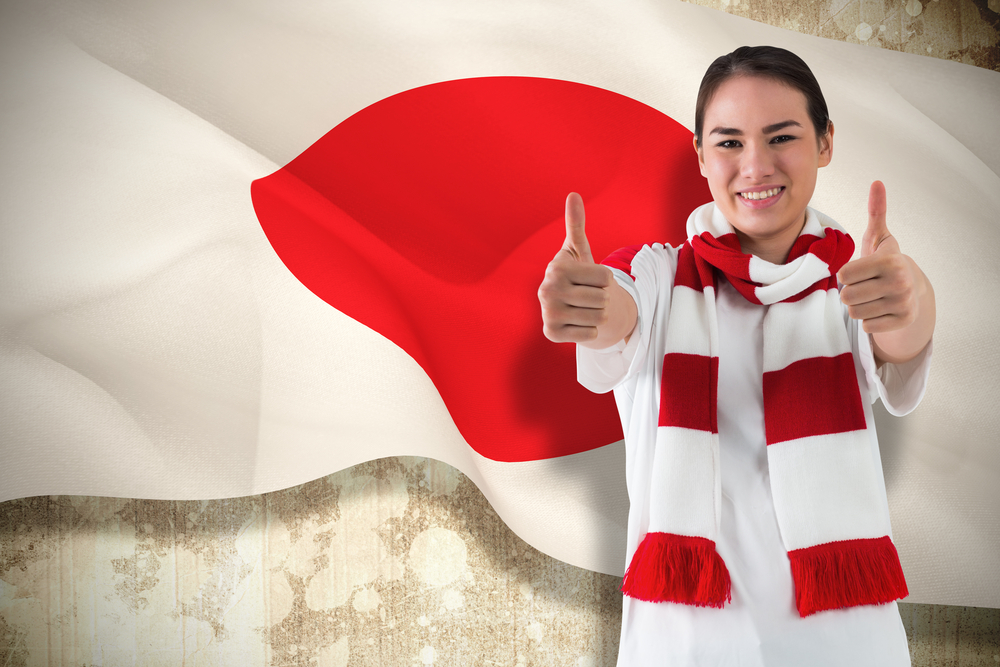 Composite image of football fan in white wearing scarf showing thumbs up against japan flag