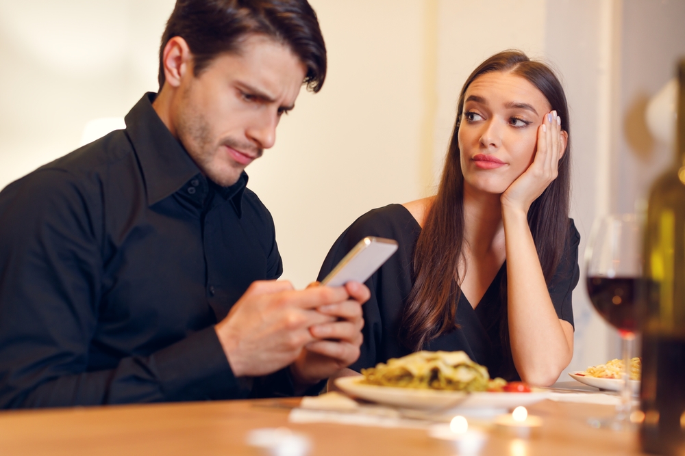 Man looking at phone instead of woman during dinner.