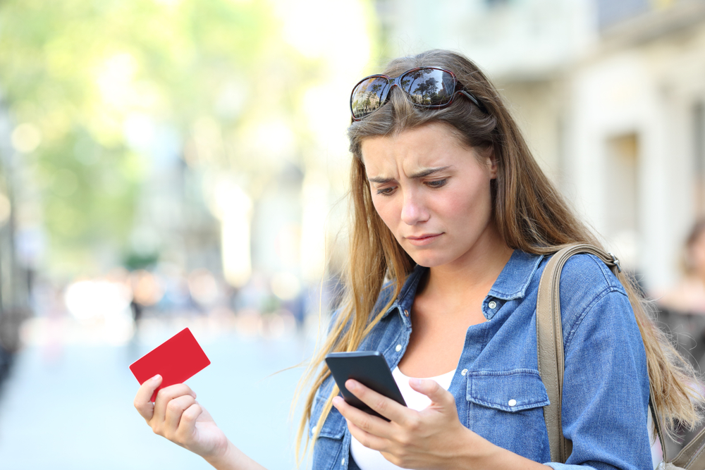 Young woman looking at phone while holding credit card in other hand.