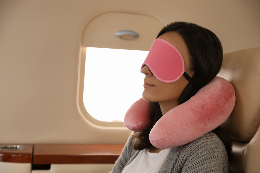 Woman on plane wearing sleeping eye mask and using pillow.