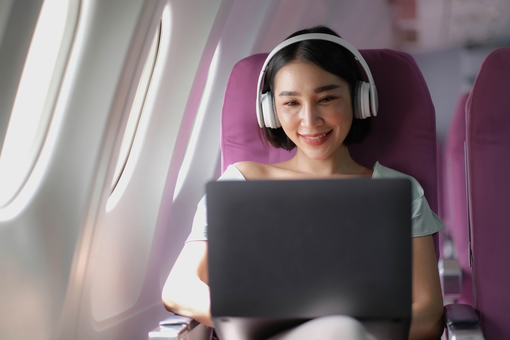 Woman on plane with headphones using a laptop.